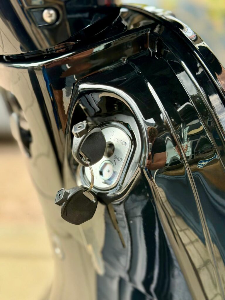 Close-up van een scooterslot met sleutel in het contact van een glanzende zwarte scooter.