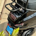 Achterkant van een glanzend zwarte scooter met bagagedrager, remlicht en blauw kenteken.