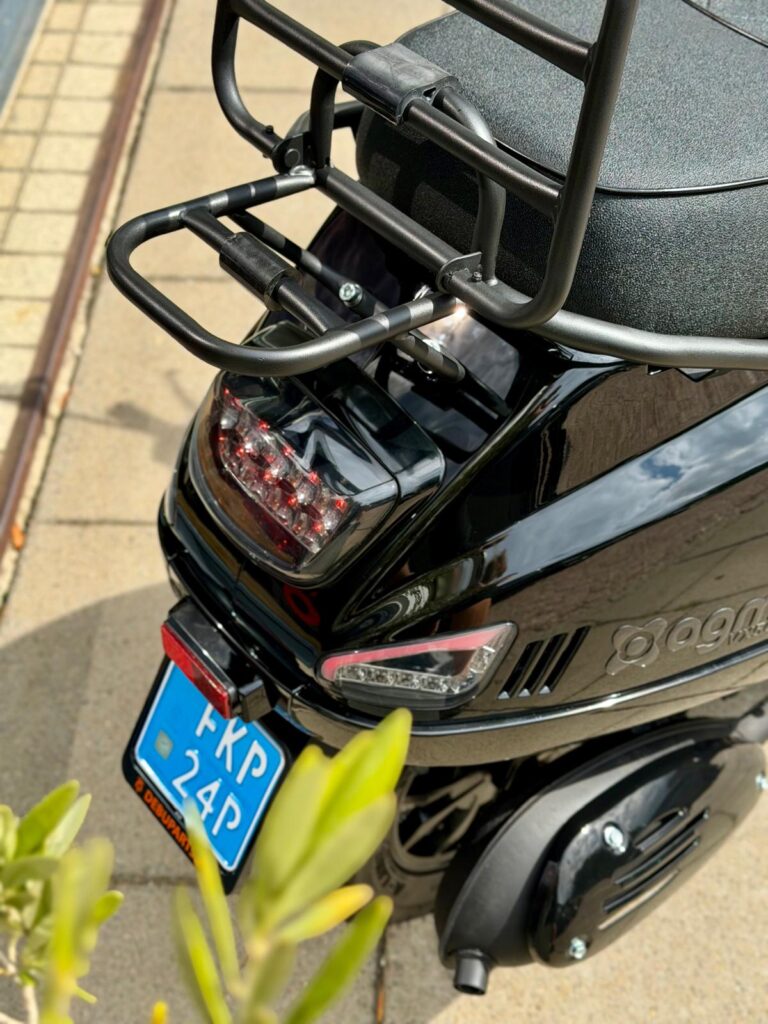 Achterkant van een glanzend zwarte scooter met bagagedrager, remlicht en blauw kenteken.