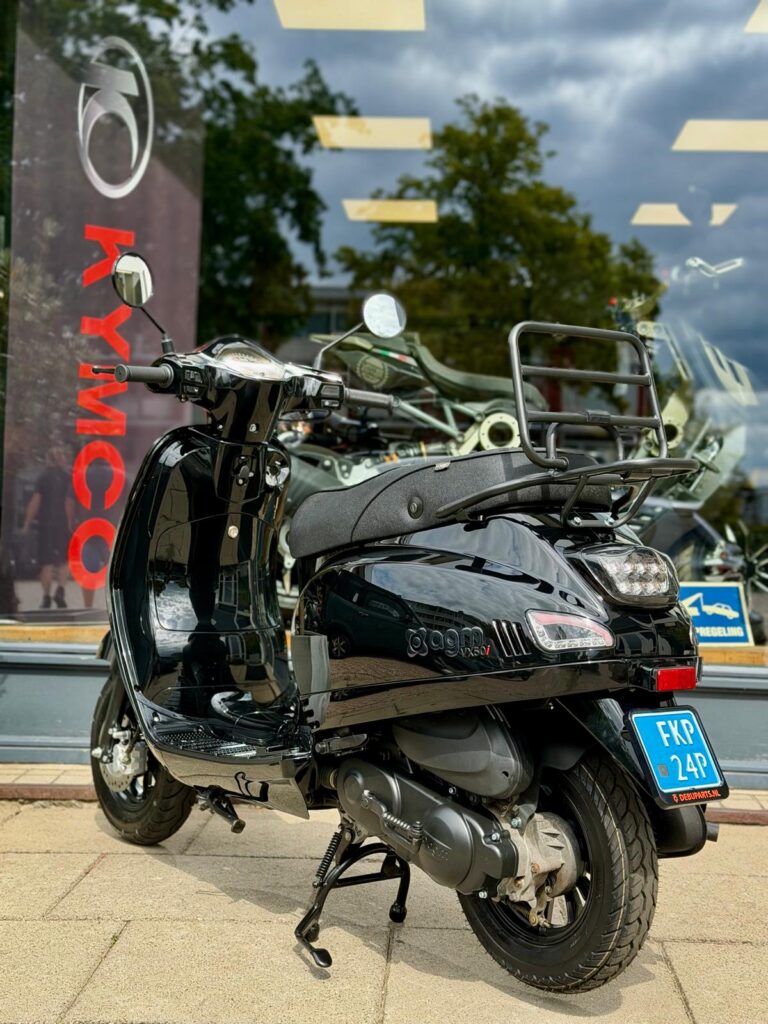Zwarte scooter op middenbok voor een winkelraam met Kymco-banner en reflecties van bomen.