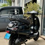 Zwarte scooter met bagagedrager geparkeerd voor werkplaats met open roldeuren.