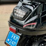 Achterkant van een zwarte scooter met LED-achterlicht, reflector en blauwe NL-kentekenplaat.
