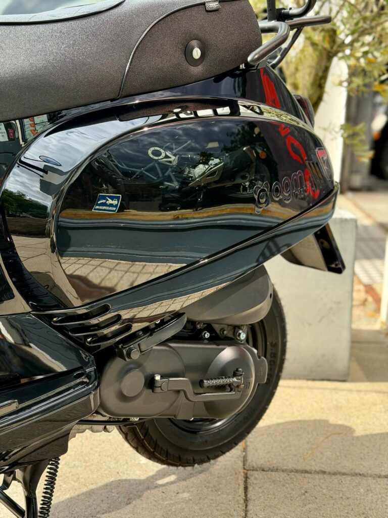 Close-up van de achterzijde van een glanzend zwarte scooter met agm-logo, motorbehuizing, achterwiel en reflecties.