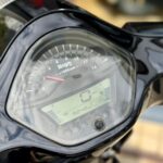 Close-up van een motorfietsinstrumentenpaneel met analoge toerenteller en digitaal display op 0 km/u.