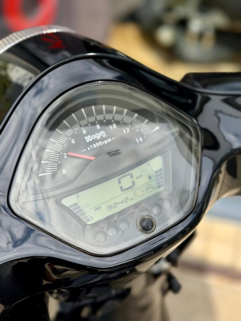 Close-up van een motorfietsinstrumentenpaneel met analoge toerenteller en digitaal display op 0 km/u.