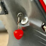 Close-up van een scootersleutel in het contact met een rode, hartvormige sleutelhanger.
