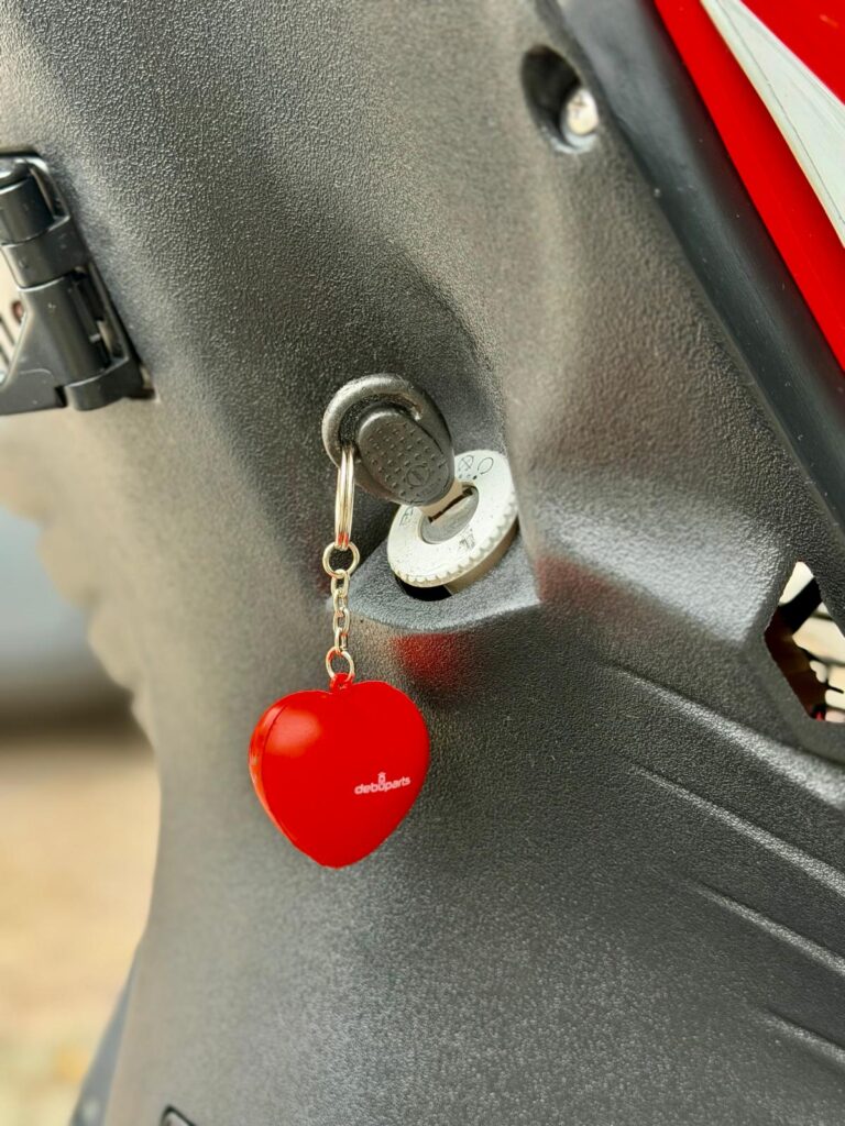 Close-up van een scootersleutel in het contact met een rode, hartvormige sleutelhanger.