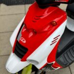 Close-up van de rood-witte voorkant van een sportieve scooter, geparkeerd op stoeptegels.