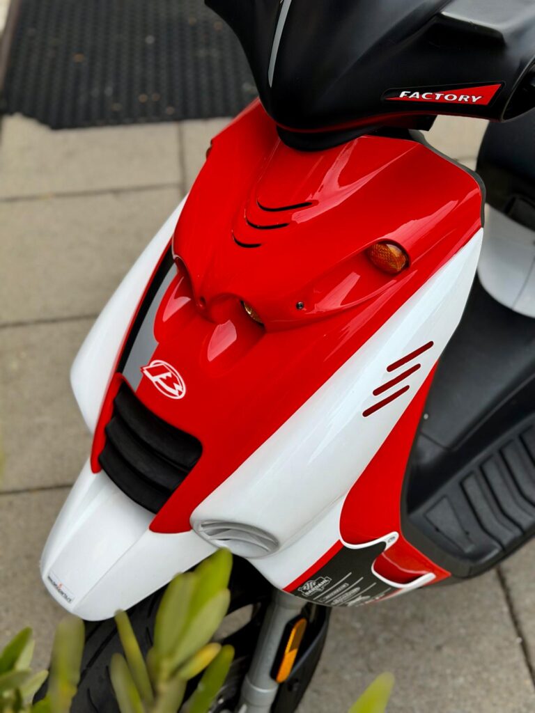 Close-up van de rood-witte voorkant van een sportieve scooter, geparkeerd op stoeptegels.