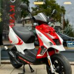 Rood-witte scooter op standaard voor een winkelraam, gezien vanaf linksvoor.