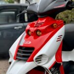 Close-up van een rode-witte sportieve scooter met koplampen en stickers, geparkeerd buiten.