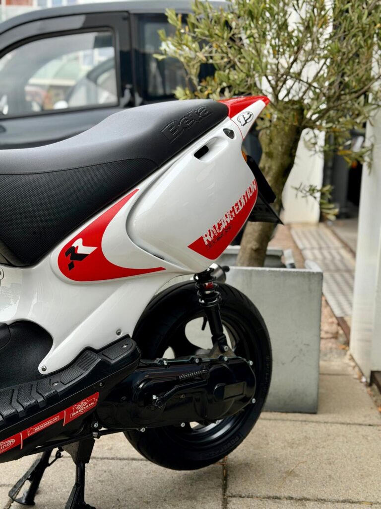 Close-up van de achterkant van een witte en rode scooter (Beta), geparkeerd naast een plantenbak.