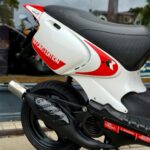 Achterzijde van een witte en rode Beta Racing Edition scooter met zwarte uitlaat, geparkeerd voor een winkelruit.