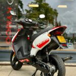 Wit-rode Kymco-scooter met Racing Edition, geparkeerd voor een winkelruit op de stoep.