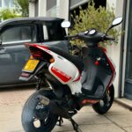 Wit-rode Racing Edition scooter op zijstandaard voor een garage, achteraanzicht met gele kentekenplaat.