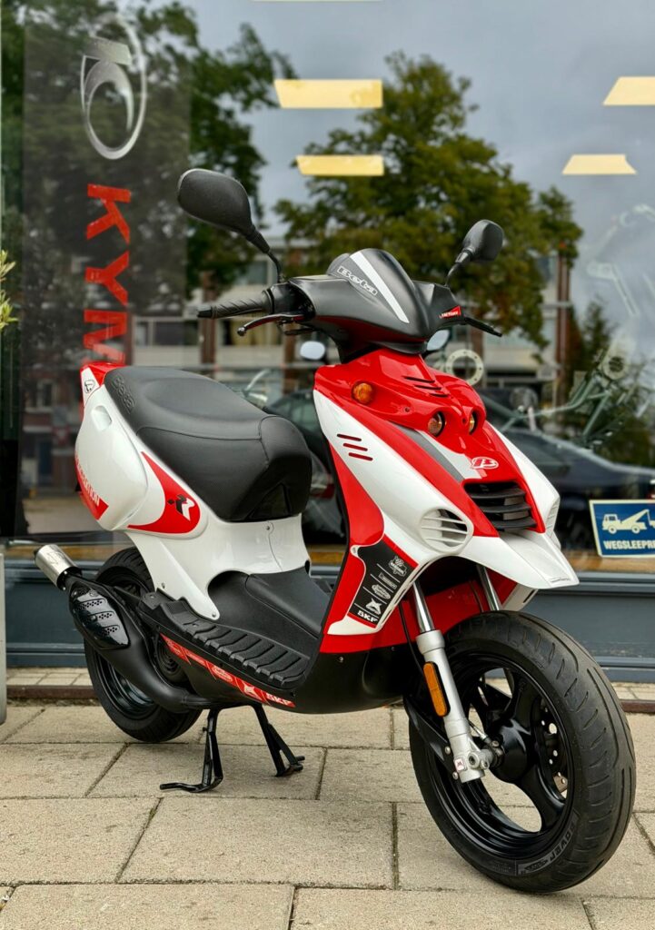 Rood-witte scooter op standaard voor een winkelraam, gezien vanaf linksvoor.