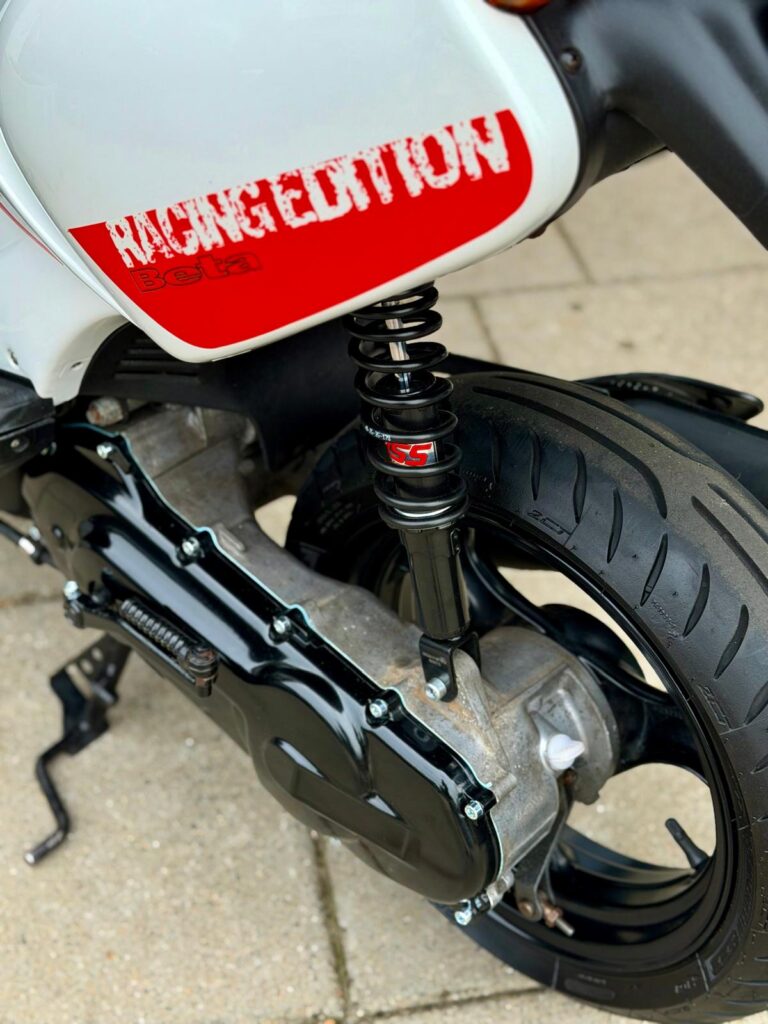 Close-up van het achterwiel en de schokdemper van een scooter met rode 'Racing Edition' sticker.