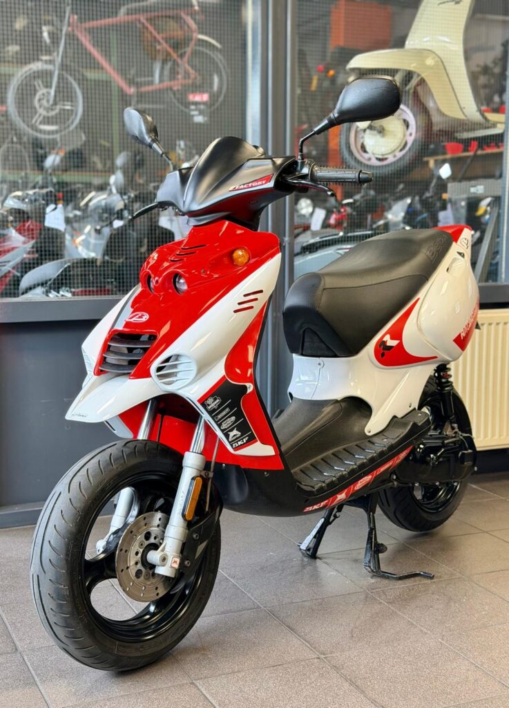 Rood-witte scooter op standaard in een showroom met andere scooters op de achtergrond.