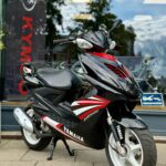 Zwarte en rode Yamaha scooter op de stoep, geparkeerd voor een winkelruit met reflecties.