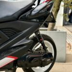 Close-up van de achterzijde van een zwarte Yamaha-scooter met witte velg, vering en zadel.