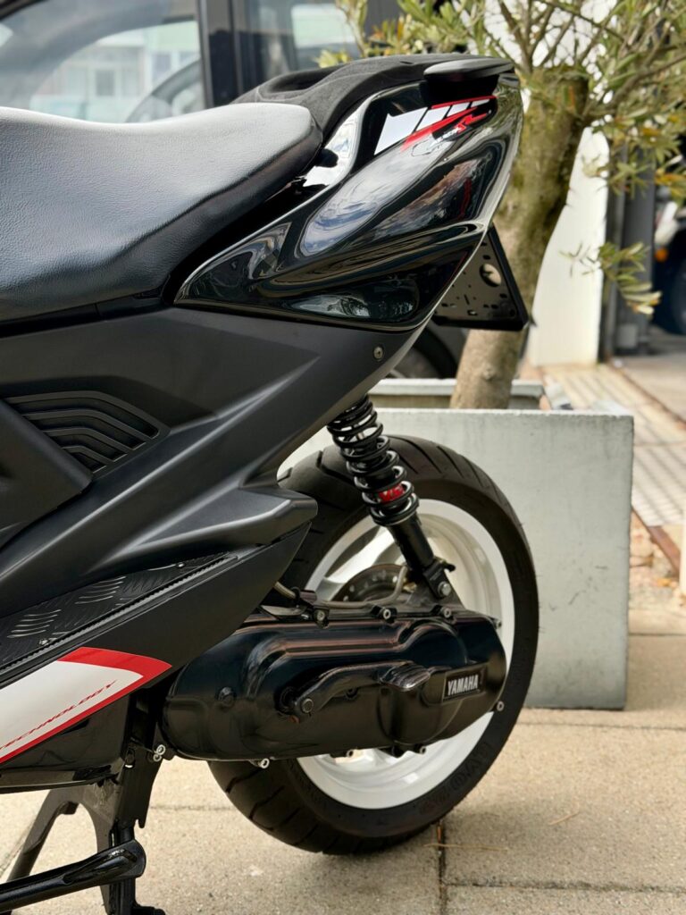 Close-up van de achterzijde van een zwarte Yamaha-scooter met witte velg, vering en zadel.