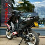 Zwarte Yamaha scooter met witte velgen, geparkeerd voor een winkel met Kymco-logo op het raam.