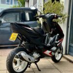 Zwarte Yamaha-scooter met witte velgen geparkeerd op stoep bij garagebox.