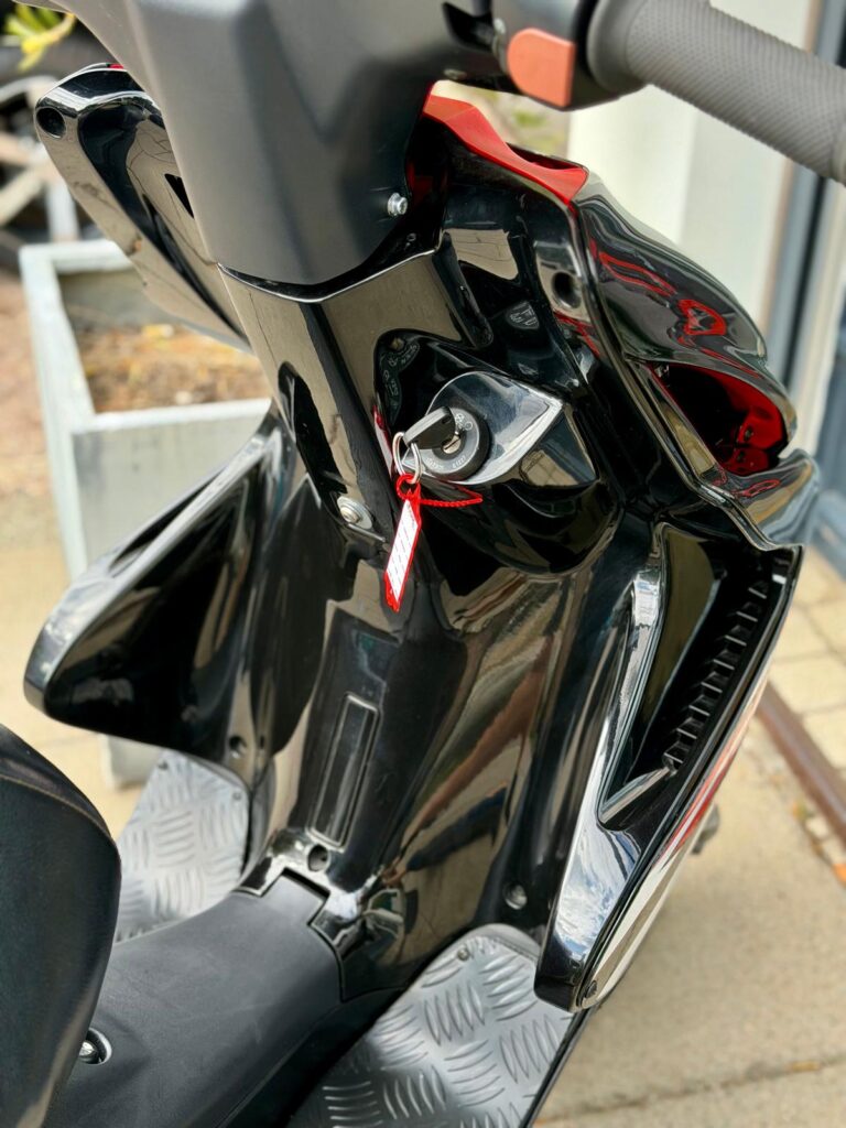 Close-up van een zwarte scooter met contactsleutel en rood sleutelhangerlabel.
