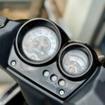 Close-up van een scooterdashboard met analoge snelheidsmeter en brandstofmeter.