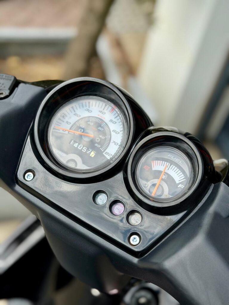 Close-up van een scooterdashboard met analoge snelheidsmeter en brandstofmeter.