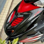 Close-up van de voorkuip van een zwarte en rode scooter met ventilatieopeningen en sportieve striping.