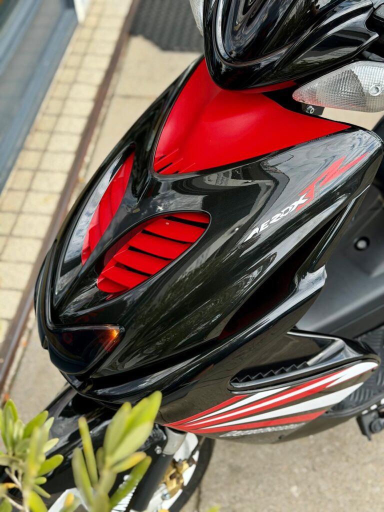 Close-up van de voorkuip van een zwarte en rode scooter met ventilatieopeningen en sportieve striping.